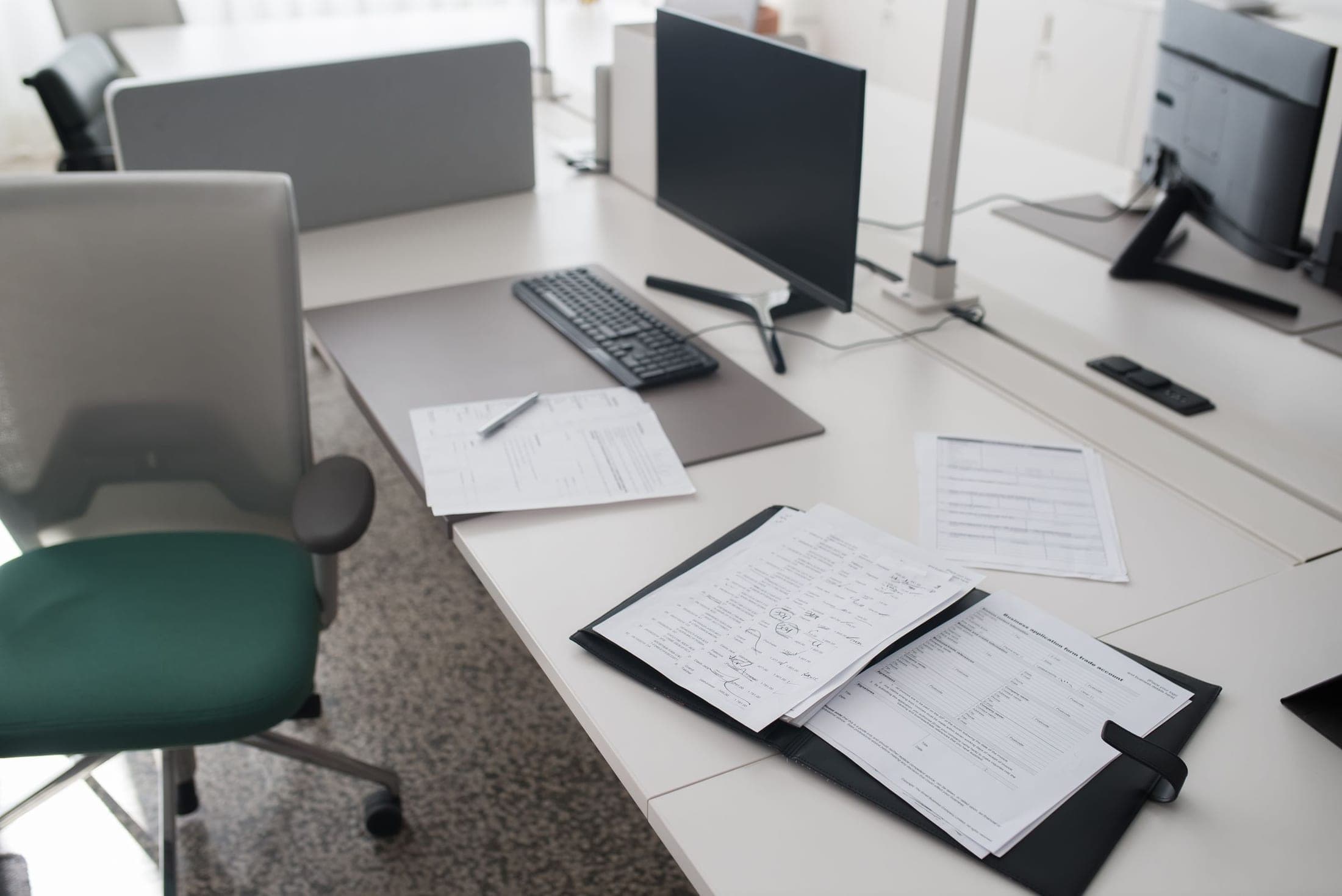 A modern office desk with a monitor, keyboard and documents in a binder